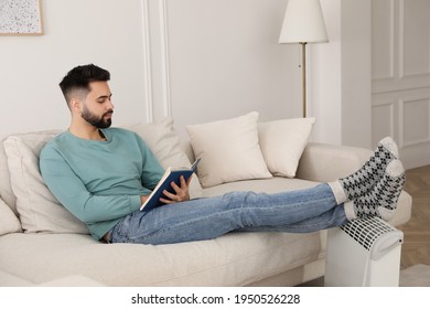 Young Man Warming Feet On Electric Heater At Home