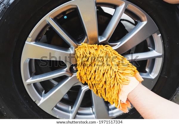 The young man washed his car with foamy cleansing\
foam. He was wearing gloves for washing the car. He wiped the\
wheels of the car.
