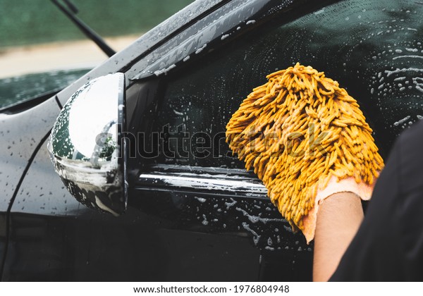 The young man washed his car with foamy cleaning\
foam. He was wearing gloves for washing the car. He wiped the side\
windows of the car.