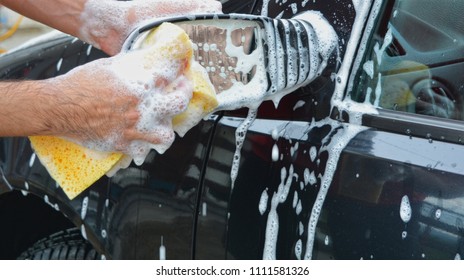 Young man washing his car in summer hot day.  Relaxing while cleaning