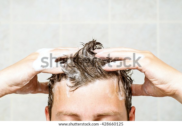 young man washing his hair,\
taking a shower with foam on his head holds fingers in hair in\
bathroom