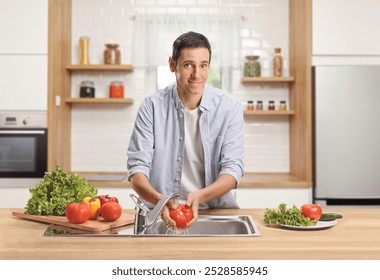 Young man washing tomato in a kitchen sink and smiling  - Powered by Shutterstock