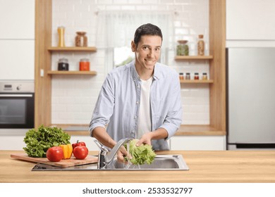 Young man washing vegetables in a kitchen sink and smiling  - Powered by Shutterstock