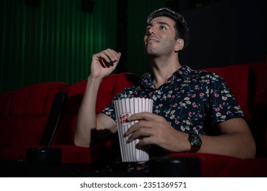 Young man watching movie and eating popcorn while sitting on red couch - Powered by Shutterstock