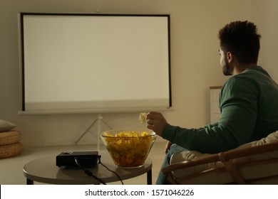 Young Man Watching Movie Using Video Projector At Home