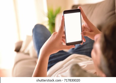 young man watching multimedia content on a smartphone vertical lying on a couch in the living room at home - Powered by Shutterstock