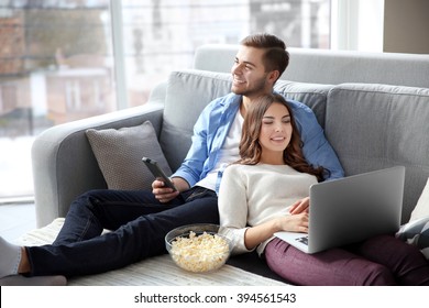 Young man watching TV and woman using laptop on a sofa at home