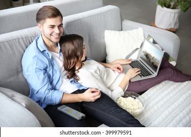 Young man watching TV and woman using laptop on a sofa at home