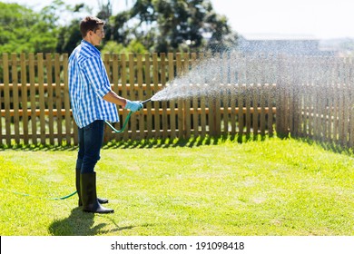 Young Man Watering Backyard Lawn Using Hosepipe