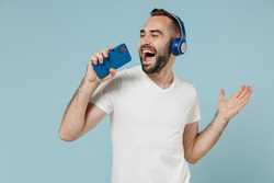 Young Man Wear Blank Print Design White T-shirt Headphones Listen To Music Sing Song Record Voice By Mobie Cell Phone Dictaphone Isolated On Plain Pastel Light Blue Color Background Studio Portrait.