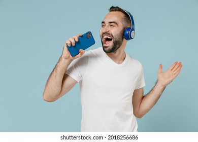 Young Man Wear Blank Print Design White T-shirt Headphones Listen To Music Sing Song Record Voice By Mobie Cell Phone Dictaphone Isolated On Plain Pastel Light Blue Color Background Studio Portrait.