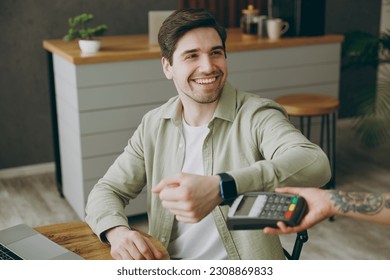 Young man wear casual clothes sits alone at table in coffee shop cafe restaurant indoors work or study on laptop pc computer hold bank terminal to process acquire smart watch payment Freelance concept - Powered by Shutterstock