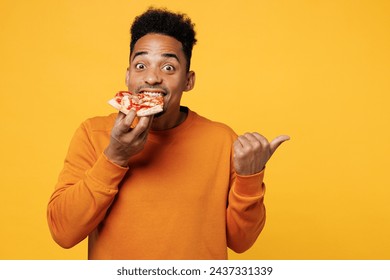 Young man wear orange sweatshirt casual clothes hold eat slice of slim italian pizza point finger aside isolated on plain yellow background. Proper nutrition healthy fast food unhealthy choice concept - Powered by Shutterstock