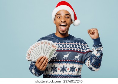 Young man wear sweater Santa hat posing hold fan of cash money in dollar banknote do winner gesture isolated on plain pastel blue background. Happy New Year 2024 celebration Christmas holiday concept - Powered by Shutterstock