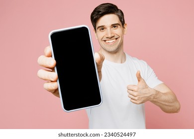 Young man wear white t-shirt casual clothes hold in hand using close up mobile cell phone in blue case with blank screen workspace area show thumb up isolated on plain pastel pink background studio - Powered by Shutterstock