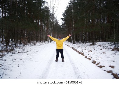 Young man weared in yellow jacket raised up his hand, standing back on the forest road in winter.