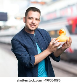 Young Man Wearing A Blue Outfit. Holding A Toy Duck. Over Train Station Background.