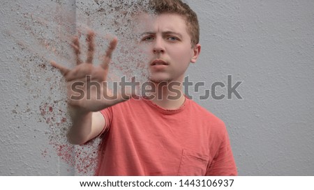 A young man wearing a bright red shirt with short hair holds out his hand desperately for help as his physical existence fades away into a million tiny particles floating away up into the sky above.