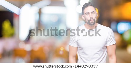 Young man wearing casual white t-shirt over isolated background making fish face with lips, crazy and comical gesture. Funny expression.