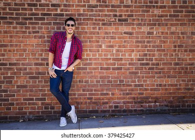 Young man wearing a check shirt and jeans against a brick wall - Powered by Shutterstock