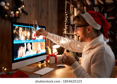 Young man wearing Christmas hat drinking champagne holding sparkler talking to friends on virtual zoom video call celebrate Happy New Year party in distance online conference chat on computer at home.