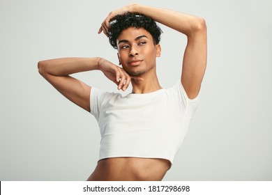 Young Man Wearing Crop Top Posing In Studio. Portrait Of A Gender Fluid Man Looking Away Against White Background.