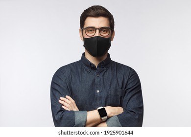 Young man wearing denim shirt, smart watch and black mask standing with crossed arms isolated on gray background - Shutterstock ID 1925901644
