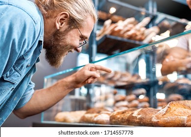 Young Man Wearing Eyeglasses Customer Standing At Bakery Shop Small Business Looking At Showcase Choosing Bread To Buy Smiling Excited