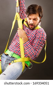 Young Man Wearing  A Fall Protection Harness And Lanyard For Work At Heights Looking Down. Gray Background