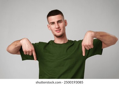 Young Man Wearing Green T-Shirt Points Downwards in Studio - Powered by Shutterstock