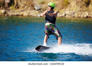 A Young Man Wearing A Helmut And Lifejacket Wakeboarding On A Lake. A Young Man Wearing A Helmet And Lifejacket Wakeboarding On A Lake.