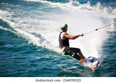 A Young Man Wearing A Helmut And Lifejacket Wakeboarding On A Lake. A Young Man Wearing A Helmet And Lifejacket Wake Boarding On A Lake.