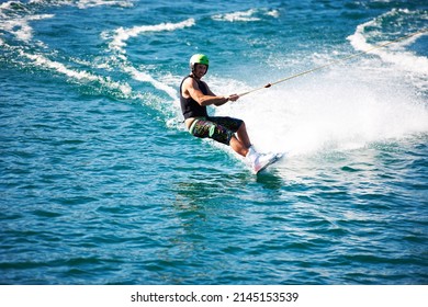 A Young Man Wearing A Helmut And Lifejacket Wakeboarding On A Lake. A Young Man Wearing A Helmet And Lifejacket Wakeboarding On A Lake.