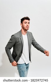 Young Man Wearing Jeans, A White Tshirt Iand A Grey Blazer Walking  In Front Of A White Wall.