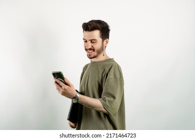 Young Man Wearing Khaki T-shirt Posing Isolated Over White Background Holding In Hands Carrying Laptop And Phone Posing. Looking At The Phone Screen.