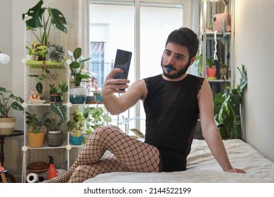Young man wearing make up, fishnet stockings and lingerie taking a selfie with the smartphone. Transgender.