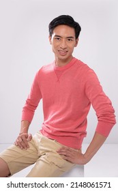 Young Man Wearing Orange Sweater With Khaki Shorts Sitting Wooden Cube Posing In Studio