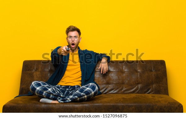 young man wearing pajamas and sitting on a sofa\
with a remote control