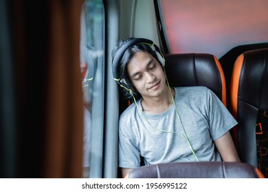 a young man wearing sleep headphones is leaning against the window while sitting by the window on a bus trip - Powered by Shutterstock