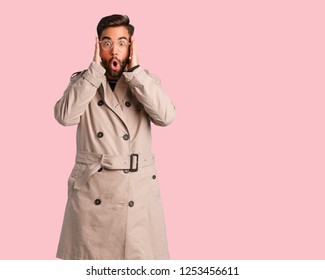 Young Man Wearing Trench Coat Surprised And Shocked