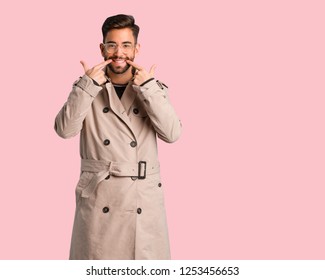 Young Man Wearing Trench Coat Smiles, Pointing Mouth