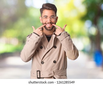 Young Man Wearing Trench Coat Smiles, Pointing Mouth