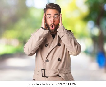 Young Man Wearing Trench Coat Surprised And Shocked