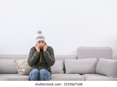 Young Man Wearing Warm Clothes Freezing On Sofa At Home. Air Conditioner Malfunction