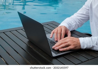 Young Man Wearing White Linen Shirt Working On His Laptop By The Pool. Male Travel Blogger Typing On Keyboard. Perks Of Being A Freelancer. Close Up, Copy Space, Background.