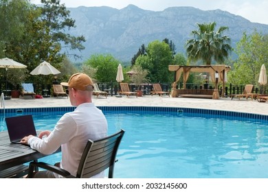 Young Man Wearing White Linen Shirt Working On His Laptop By The Pool. Male Travel Blogger Typing On Keyboard. Perks Of Being A Freelancer. Close Up, Copy Space, Background.