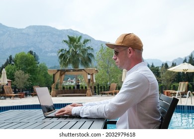 Young Man Wearing White Linen Shirt Working On His Laptop By The Pool. Male Travel Blogger Typing On Keyboard. Perks Of Being A Freelancer. Close Up, Copy Space, Background.