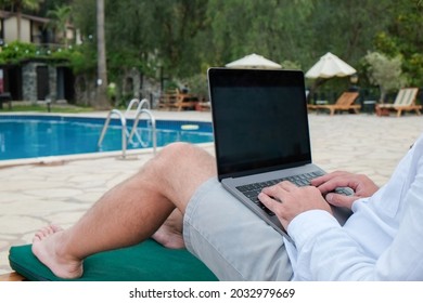 Young Man Wearing White Linen Shirt Sitting On The Deck Chair, Working On His Laptop By The Pool. Male Travel Blogger Typing On Keyboard. Perks Of Being A Freelancer. Close Up, Copy Space, Background.