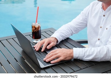 Young Man Wearing White Linen Shirt Working On His Laptop By The Pool. Male Travel Blogger Typing On Keyboard. Perks Of Being A Freelancer. Close Up, Copy Space, Background.