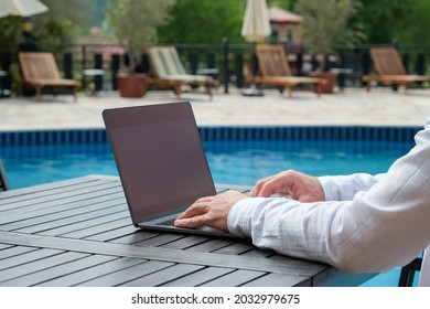 Young Man Wearing White Linen Shirt Working On His Laptop By The Pool. Male Travel Blogger Typing On Keyboard. Perks Of Being A Freelancer. Close Up, Copy Space, Background.